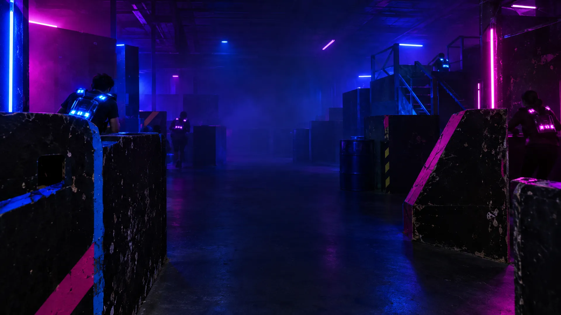 Players in glowing vests moving between black barriers in a laser tag arena lit blue and magenta